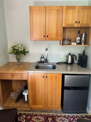 Una cocina compacta con armarios de madera, un lavamanos de acero inoxidable, cafetera y lavavajillas.