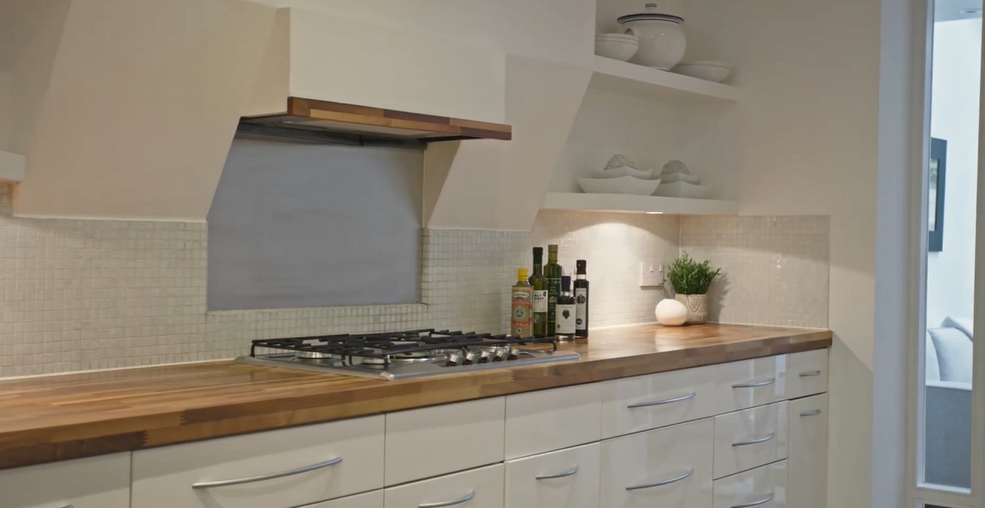 Una cucina moderna con piano cottura a gas, mobili bianchi e un bancone in legno.