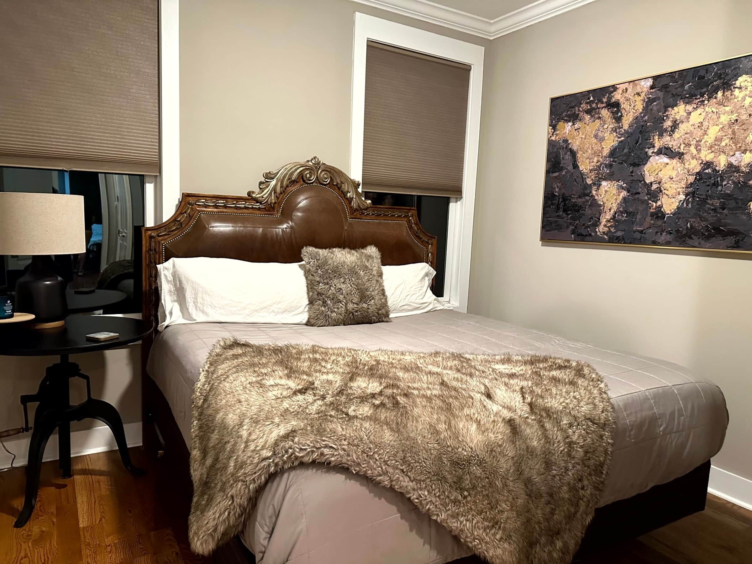 Een slaapkamer met een groot bed, een nachtkastje, een lamp, een wereldkaart aan de muur en een raam met een luxaflex.