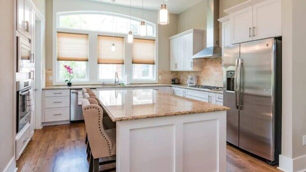 A modern kitchen with white cabinetry, a stainless steel refrigerator, and a large island with a granite countertop. - MusikHouse East I Rooftop + Hot Tub I 5 mi to DWNT (Nashville)