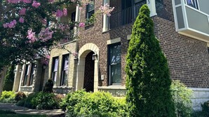 A multi-story brick building with a balcony, a well-maintained lawn, and flowering trees. - MusikHouse East I Rooftop + Hot Tub I 5 mi to DWNT (Nashville)
