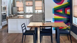 A modern kitchen with a large island, pendant lighting, and a colorful abstract wall. - MusikHouse East I Rooftop + Hot Tub I 5 mi to DWNT (Nashville)