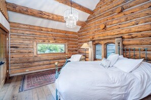 Ein Schlafzimmer in einer Blockhütte mit einem Bett, einem Fenster und einer Chandelüster.