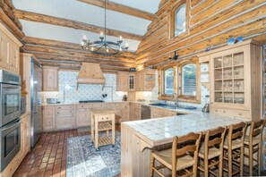 Eine Kücheneinrichtung im Chalet-Stil mit Holzausstattung, einer zentralen Kochinsel und einer Kristallleuchter.