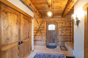 Ein rustikales Holzhaus-Interieur mit Holztür, Treppe und einer Kronleuchter.