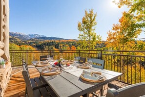 Eine Holzterrasse mit Esstisch, mit Blick auf eine gebirgige Landschaft.