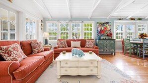 A spacious living room with a red sofa, a white coffee table, and a dining area with a green table and chairs. - Captiva Home New to Rental Market ! (Captiva)