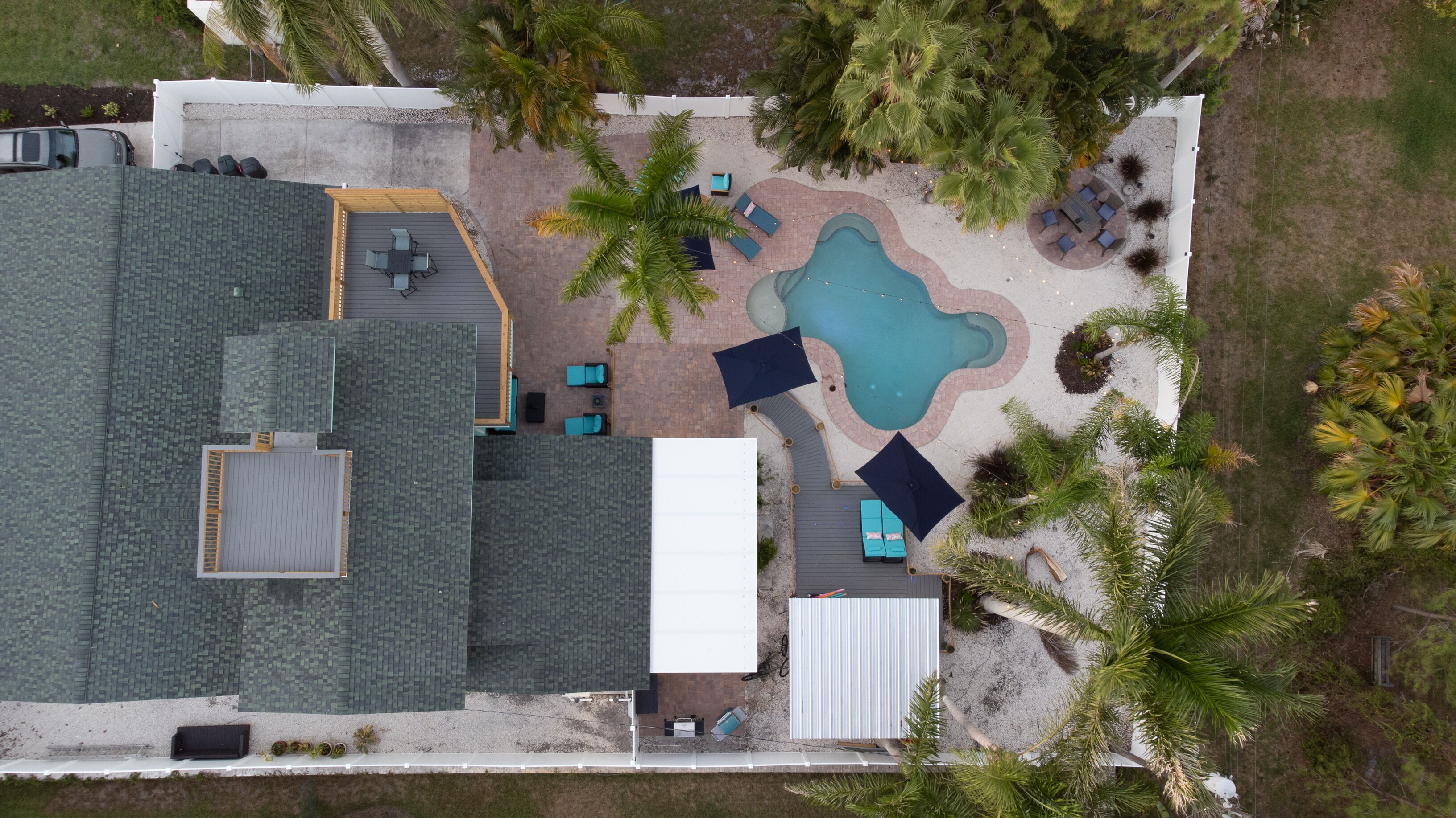 An aerial view of a residential property with a swimming pool, patio furniture, and a garage.