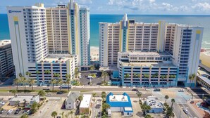A high-rise hotel with multiple floors, a parking area, and a view of the beach.