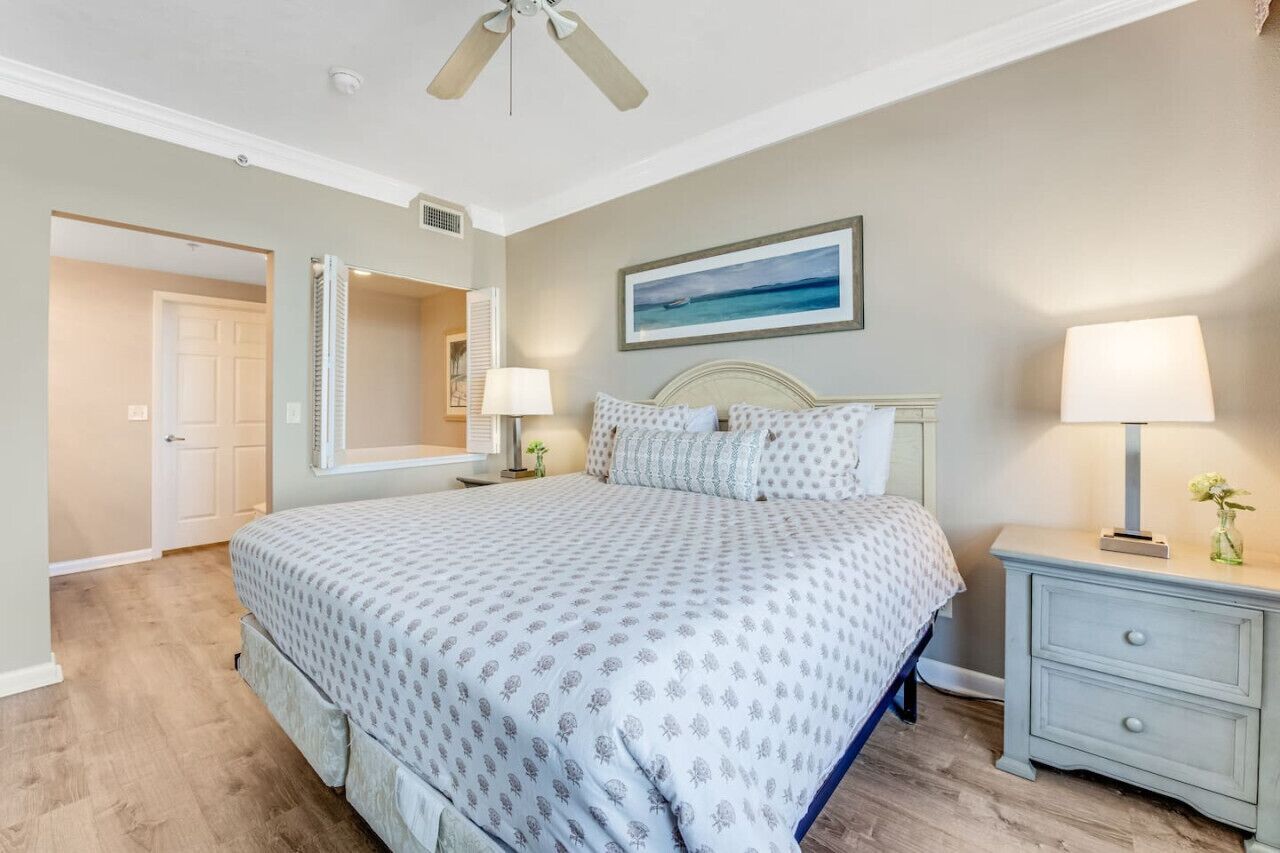 A bedroom with a bed, nightstand, lamp, and a painting on the wall.