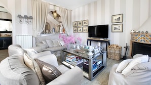 A living room with striped wallpaper, a sofa, a coffee table with books, a television, and a fireplace. - Appartamento Terrazza Tasso (Sorrento)