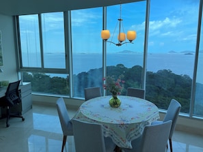 Un'area pranzo con tavolo apparecchiato per quattro, un vaso con fiori e vista sul mare e sul verde.