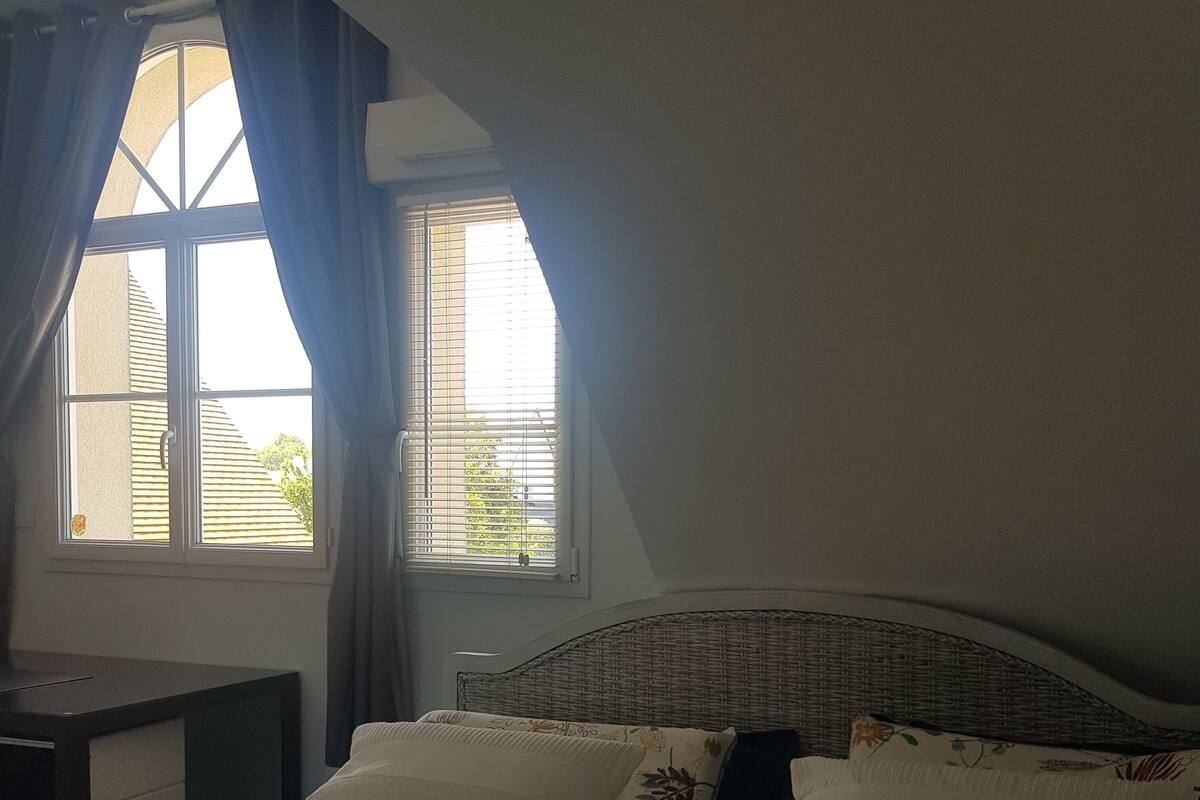 A bedroom with a bed, a nightstand, a window with curtains, and a view of greenery outside.