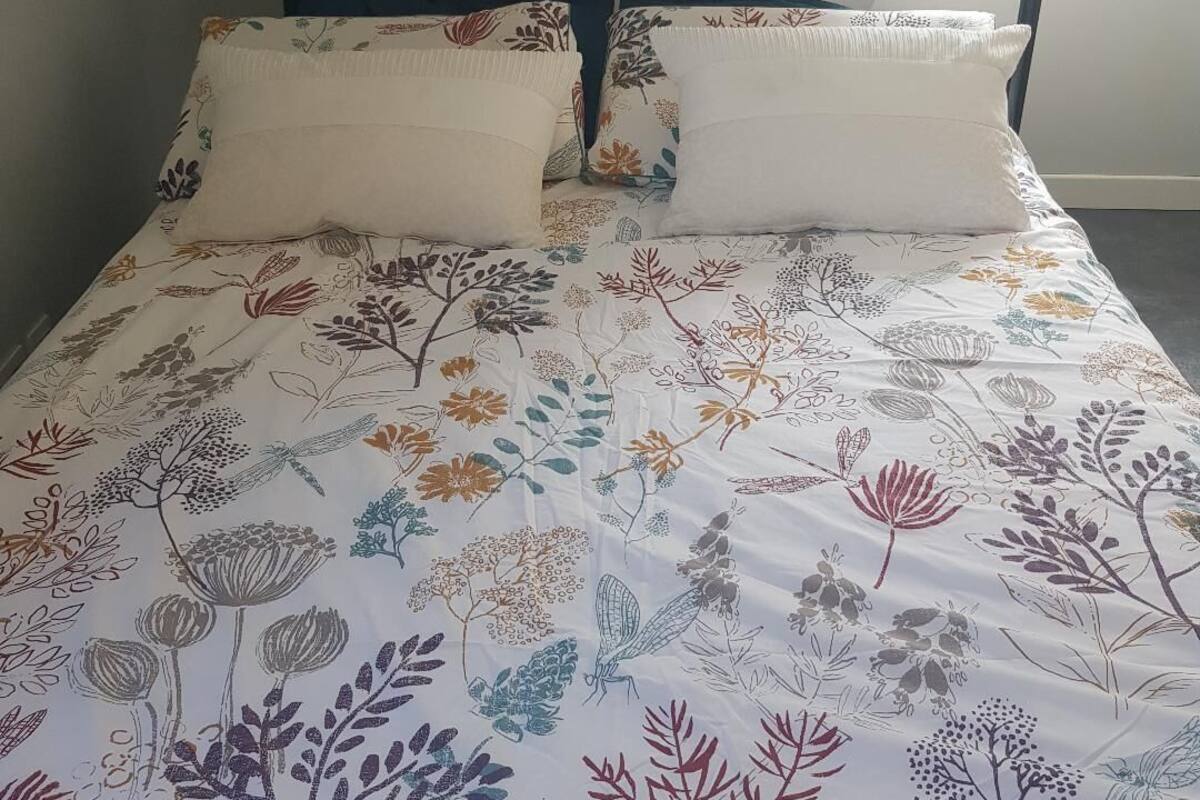 A bed with a floral-patterned bedspread and two pillows, a black metal headboard, and a window with natural light.