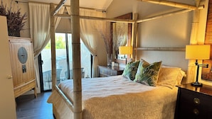 Una cama con dosel, un armario de madera, una mesita de noche con lámpara y vistas al exterior.