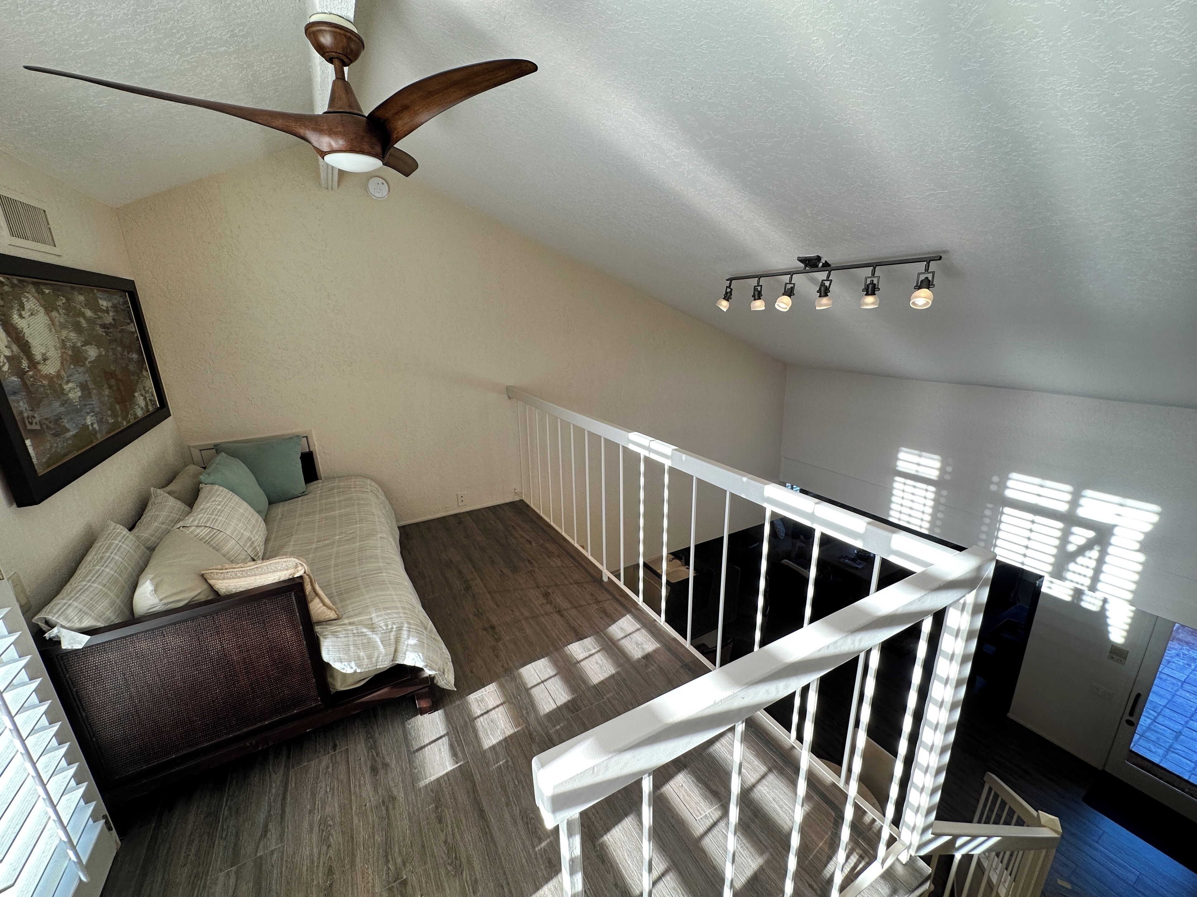 A bedroom with a bed, a ceiling fan, a window, and a staircase.