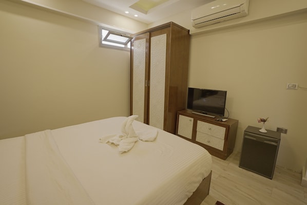 A hotel room with a bed, a TV, a mini-fridge, and a wardrobe.