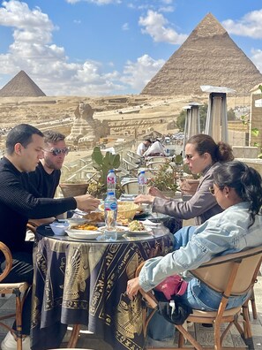 A group of people dining at a table with a view of pyramids in the background.