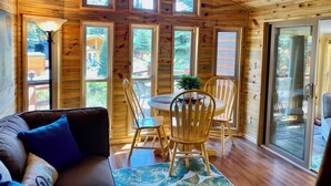 A cozy cabin interior with a wooden interior, a dining area with a table and chairs, and large windows offering views of the outdoors.