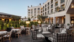Un patio de hotel con mobiliario exterior, una piscina y un edificio con varios balcones.