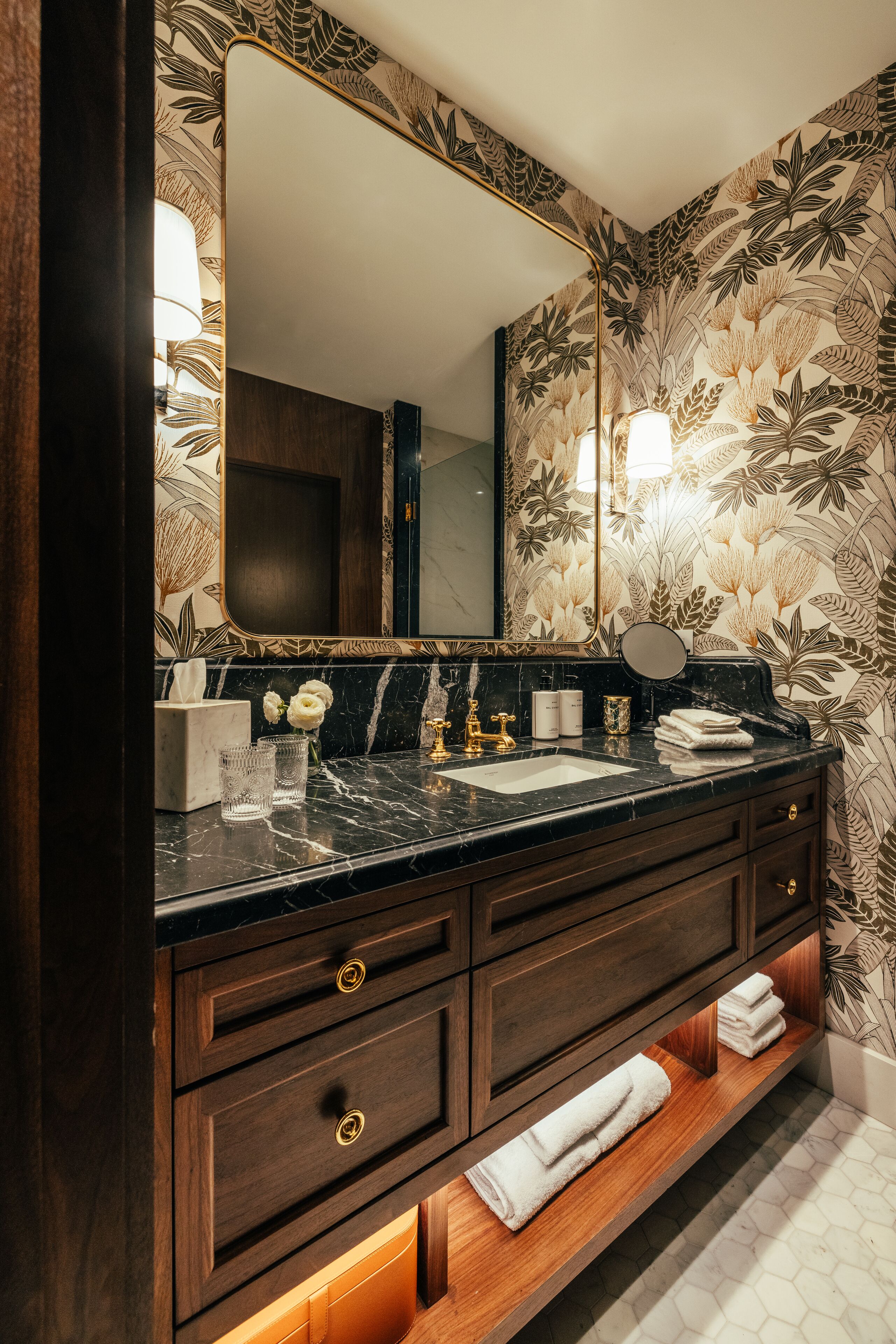A bathroom with a dark wood vanity, a large mirror, and a floral wallpaper design.