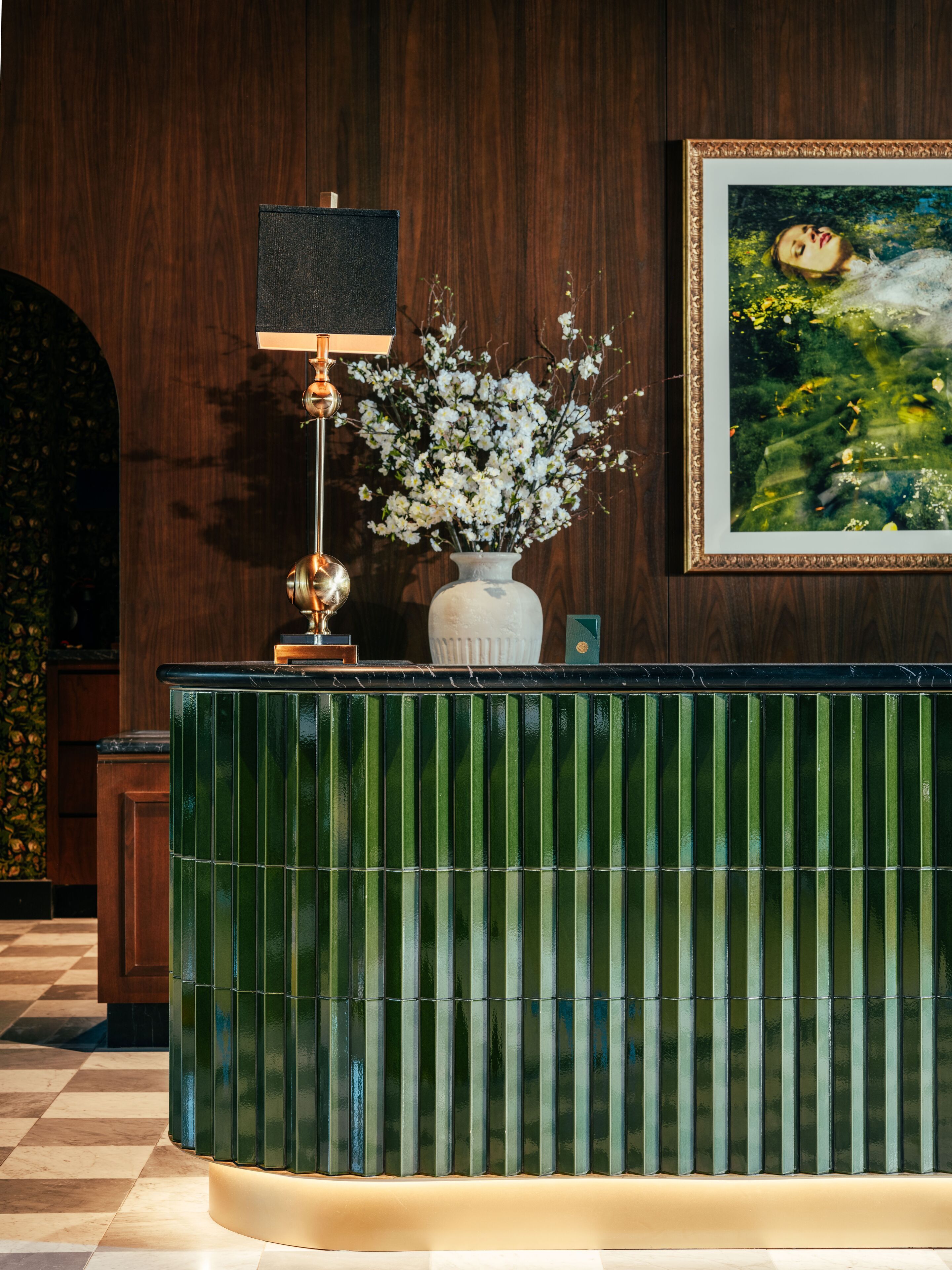 Una recepción con un diseño verde estampado, un jarrón con flores blancas y un cuadro en la pared.