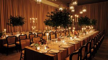 A long banquet table set for a formal event, with chairs on both sides, candles, and floral centerpieces.