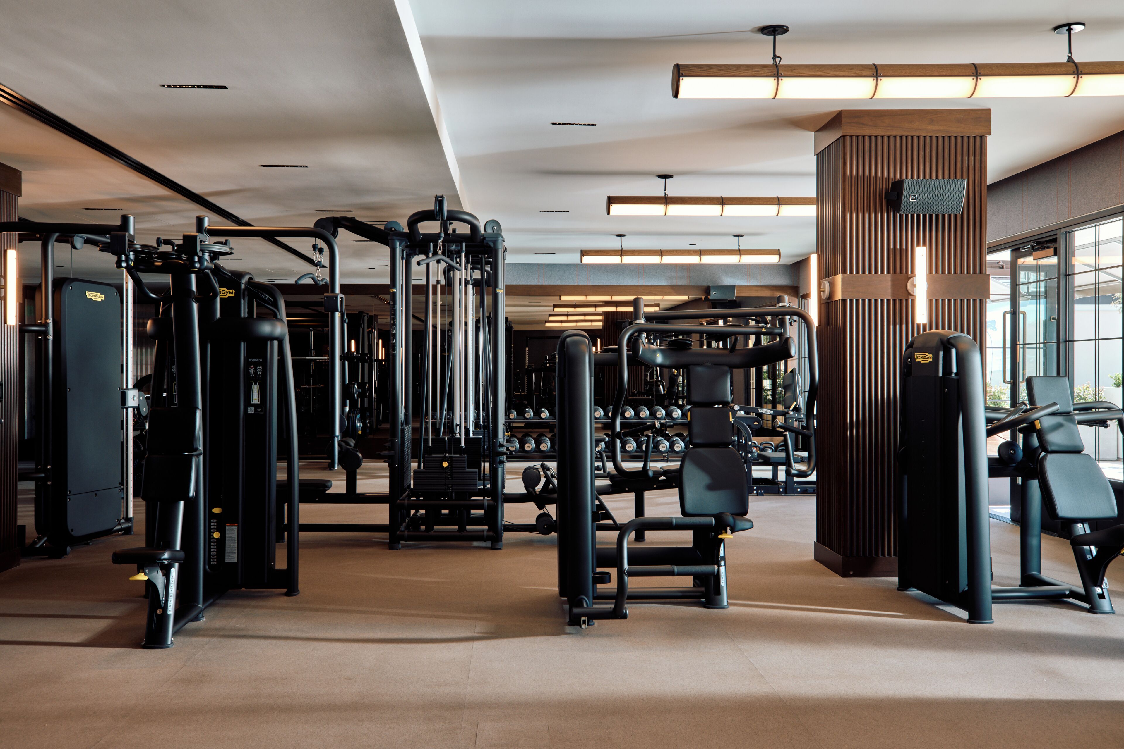 Un gimnasio con diversas máquinas de ejercicio, un soporte para pesas y un amplio ventanal que proporciona luz natural.