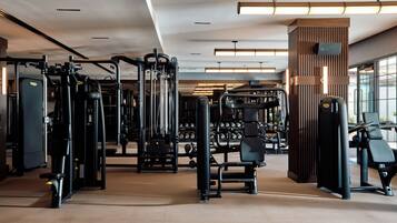Un gimnasio con diversas máquinas de ejercicio, un soporte para pesas y un amplio ventanal que proporciona luz natural.