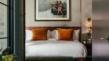 A modern hotel room with a large bed, two pillows, a framed artwork above the bed, a bedside table with a lamp, and a view of the outside through a glass door.