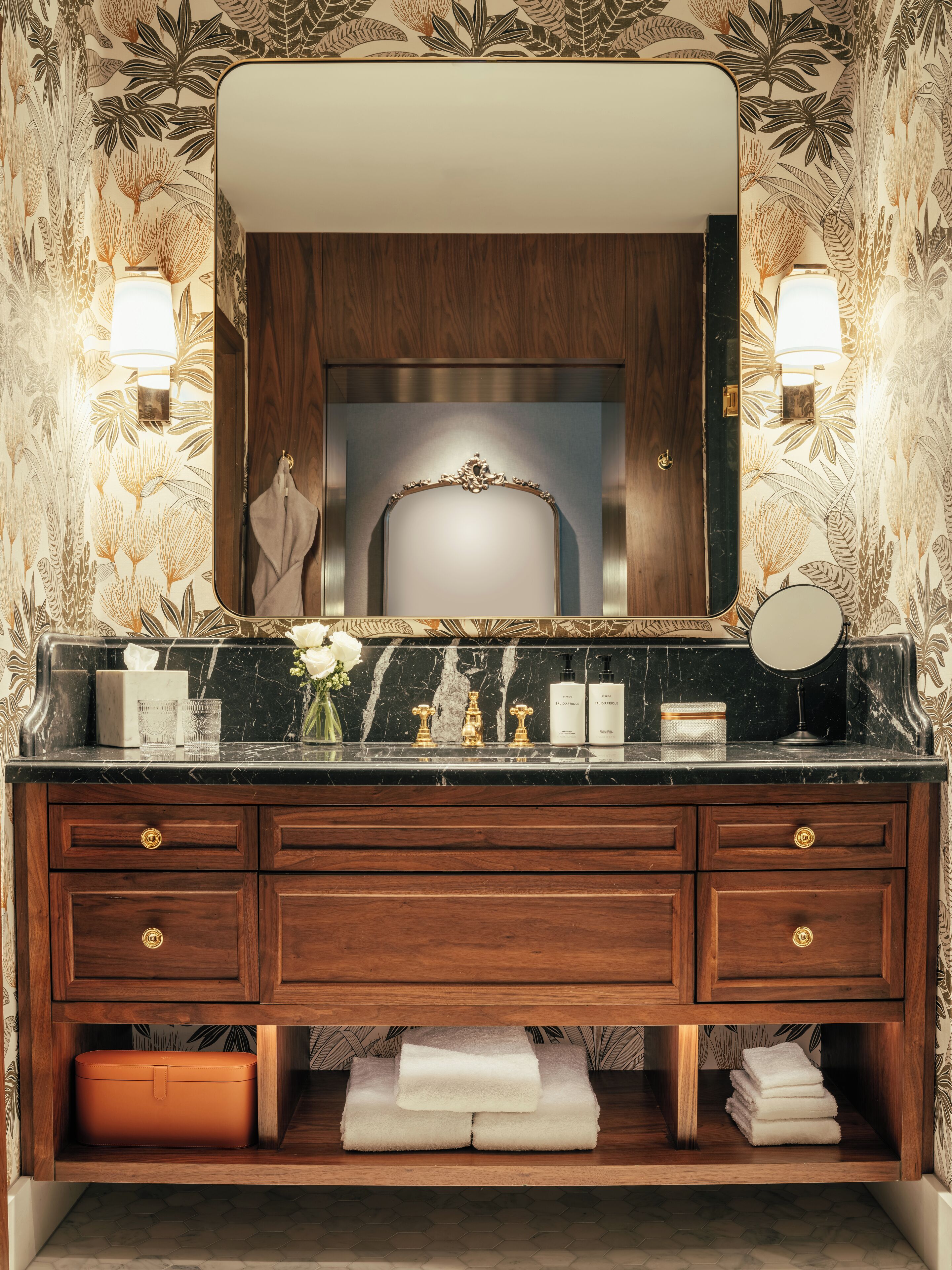 A bathroom vanity with a mirror, two wall-mounted lights, a marble countertop, and a wooden cabinet with drawers.
