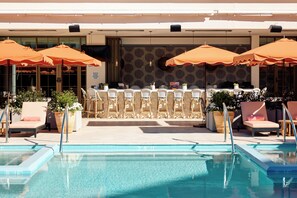 Ein Poolbereich mit Liegestühlen und Sonnenschirmen, eine Bar mit Sitzgelegenheiten sowie Kübelpflanzen.
