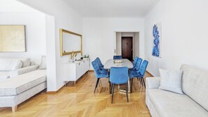 A modern living room with a dining area, white furniture, and a herringbone wood floor.