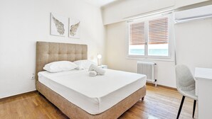 A bedroom with a bed, a bedside table, a chair, a window with blinds, and a radiator.