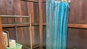 A small bathroom with a wooden floor, a white toilet, a blue shower curtain, and a metal shelf with green baskets.