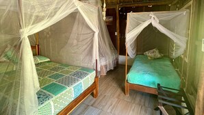 A room with two wooden beds, each with a mosquito net, and a thatched roof.