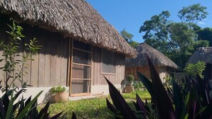 A traditional thatched-roof house with a wooden exterior, a sliding door, and a small garden area with potted plants.
