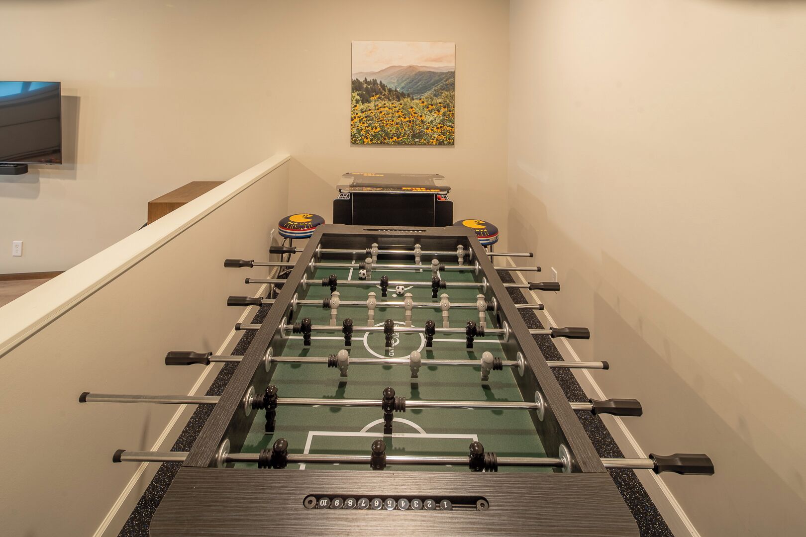 Een tafelvoetbaltafel in een ruimte met een schilderij aan de muur en een aan de muur bevestigde televisie.