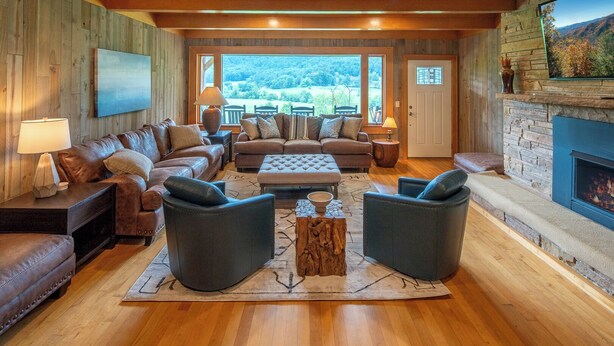Ein gemütliches Wohnzimmer mit Ledersofas, einem Kamin und einem großen Fenster mit herrlichem Ausblick.