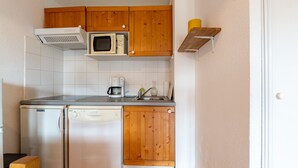 Cocina compacta con armarios de madera, microondas, cafetera y lavavajillas.