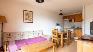 Un espacio habitable compacto con sofá, una mesa de comedor con sillas, zona de cocina con microondas y televisor.