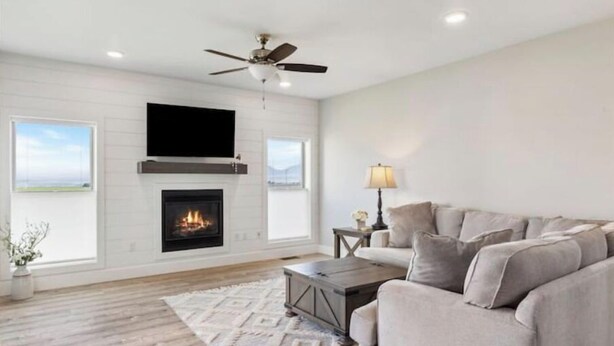 A modern living room with a fireplace, a ceiling fan, and a large window. - Townhome Near Bozeman Airport (Belgrade)