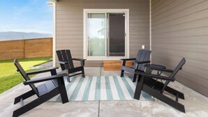 A covered patio with four black chairs, a striped rug, and a sliding glass door. - Townhome Near Bozeman Airport (Belgrade)