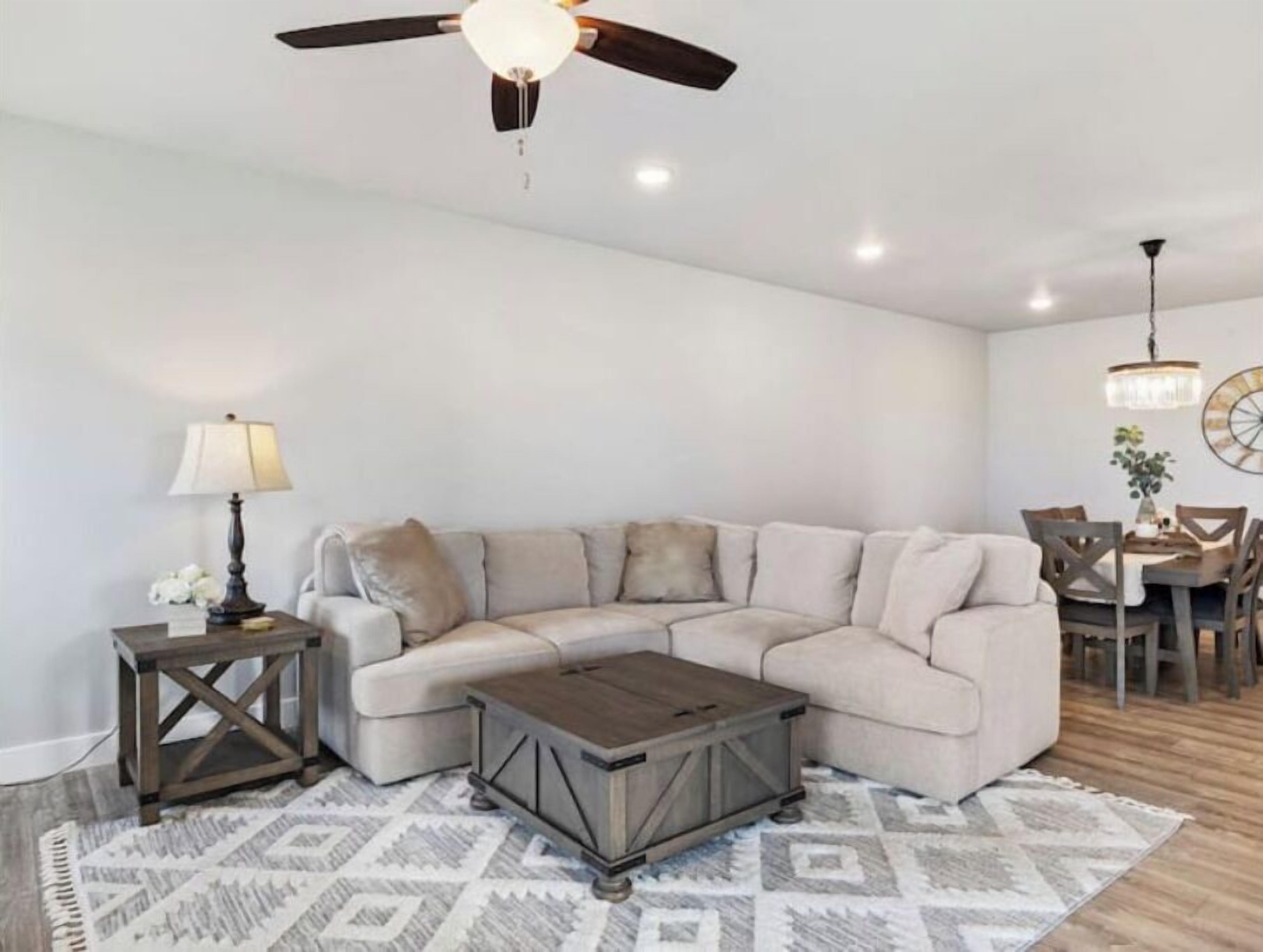 A living room with a sectional sofa, a coffee table, a lamp, and a ceiling fan.