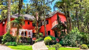Un edificio rojo con techo de tejas, rodeado de árboles y un jardín bien cuidado.
