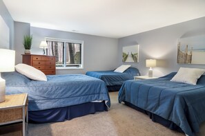 A bedroom with two beds, a dresser, a lamp, and a window with blinds.