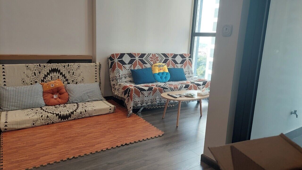 Sala de estar con dos sofás, uno con funda estampada y el otro con diseño geométrico. Hay una mesita redonda pequeña con un control remoto encima.