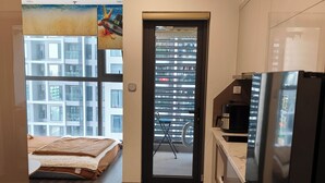 Ein kleines Hotelzimmer mit Bett, einer Kochnische und Blick auf die Stadt.