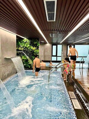 Ein Schwimmbad mit Wasserfall, umgeben von einer gefliesten Terrasse und Innenwänden.