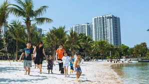 Ein Strand mit Menschen, Palmen und Hochhäusern im Hintergrund.